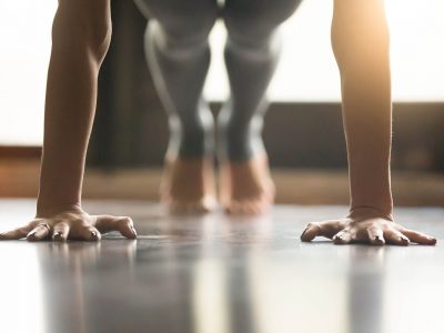 Young yogi woman standing in Plank pose, home interior backgroun Young woman practicing yoga, doing Push ups or press ups exercise, phalankasana Plank pose, working out, wearing sportswear, grey pants, indoor, home interior, living room floor. Close-up of hands